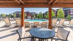 A poolside area with lounge chairs and a table, overlooking a pool and buildings in the background.