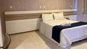 A neatly made bed with white bedding and a dark blue accent, a wooden headboard, and a tiled floor. - Farol Plaza Hotel (Aracaju)