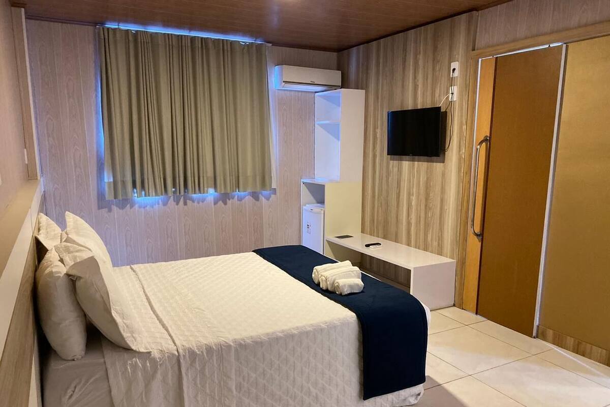 Hotellihuone, jossa on sänky, yöpöytä, televisio ja vaatekaappi.