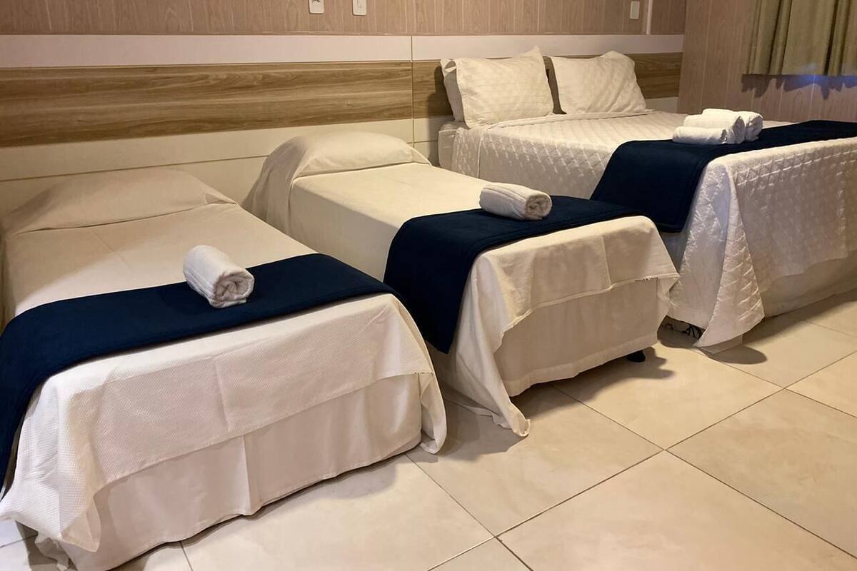 Hotellihuone, jossa on kolme sängyä rivissä, ja jokaisessa sängyssä on valkoinen päiväpeite ja tummansininen peitto.
