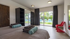 Ein modernes Hotelzimmer mit einem großen Bett, einem Kleiderschrank und einer Glastür, die zu einem Poolbereich führt.