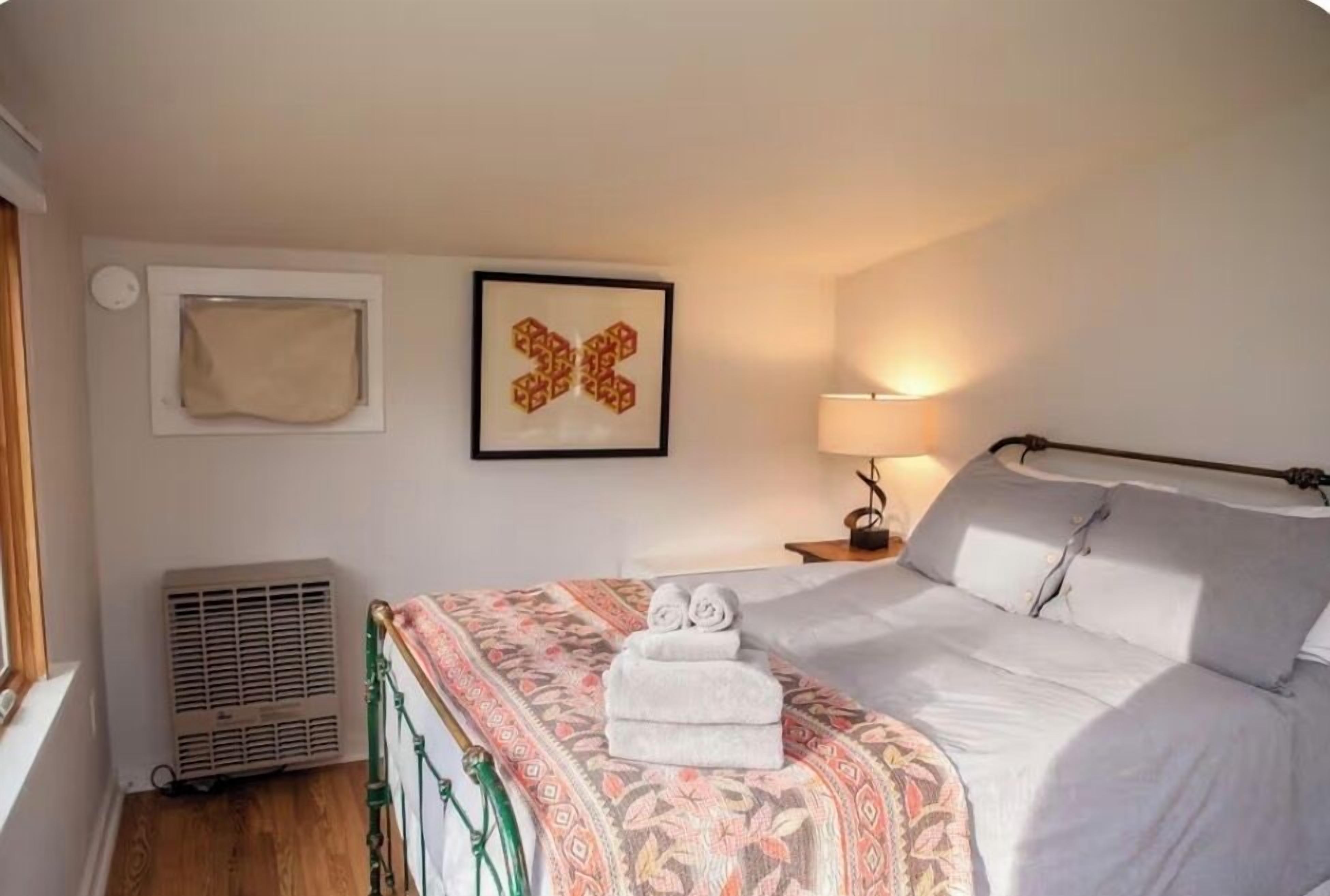 Een slaapkamer met een bed, een radiator, een wandlamp en een ingelijst kunstwerk.