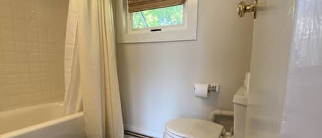 A bathroom with a bathtub, toilet, and a window with a view.