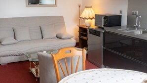 Um espaço compacto com sofá, mesa de jantar, micro-ondas, máquina de lavar louça e um pequeno armário.