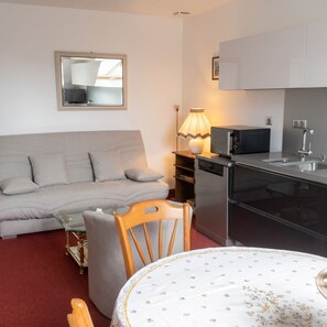 A compact living space with a sofa, a dining table, a microwave, a dishwasher, and a small cabinet. - Homerez - Cozy Apartment in Saint-Planchers (Saint-Planchers)