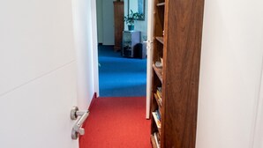 Um corredor com carpete vermelho que leva a um quarto com estante de madeira.