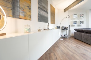 Una cocina moderna con armarios blancos, suelo de madera y un sofá gris en la sala de estar.