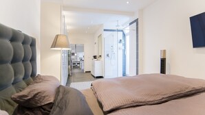 A modern hotel room with a large bed, a desk, and a bathroom visible through an open door.