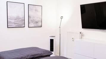 A bedroom with two beds, a ceiling light, a radiator, and a TV mounted on the wall.