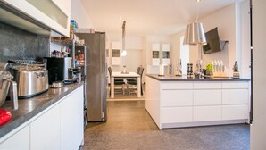 A modern kitchen with a central island, a dining area, and a TV mounted on the wall.