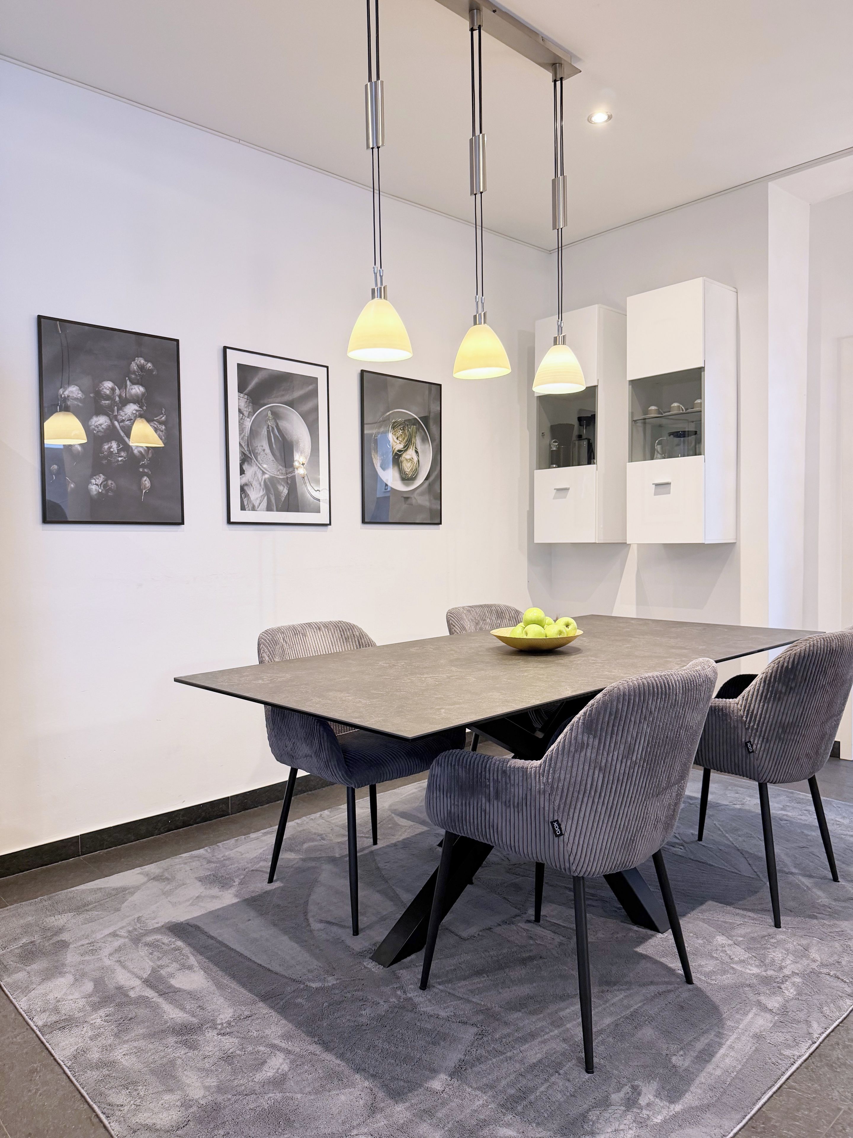 A modern dining area with a rectangular table, six upholstered chairs, and pendant lighting.