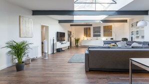 A modern living room with a grey sofa, a TV, and a skylight above.
