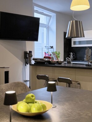 A modern kitchen with a flat-screen TV, a dining table with chairs, and a bowl of green apples.
