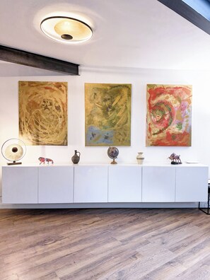 Un interior moderno con una consola blanca que exhibe objetos decorativos, una lámpara de techo y arte abstracto en la pared.