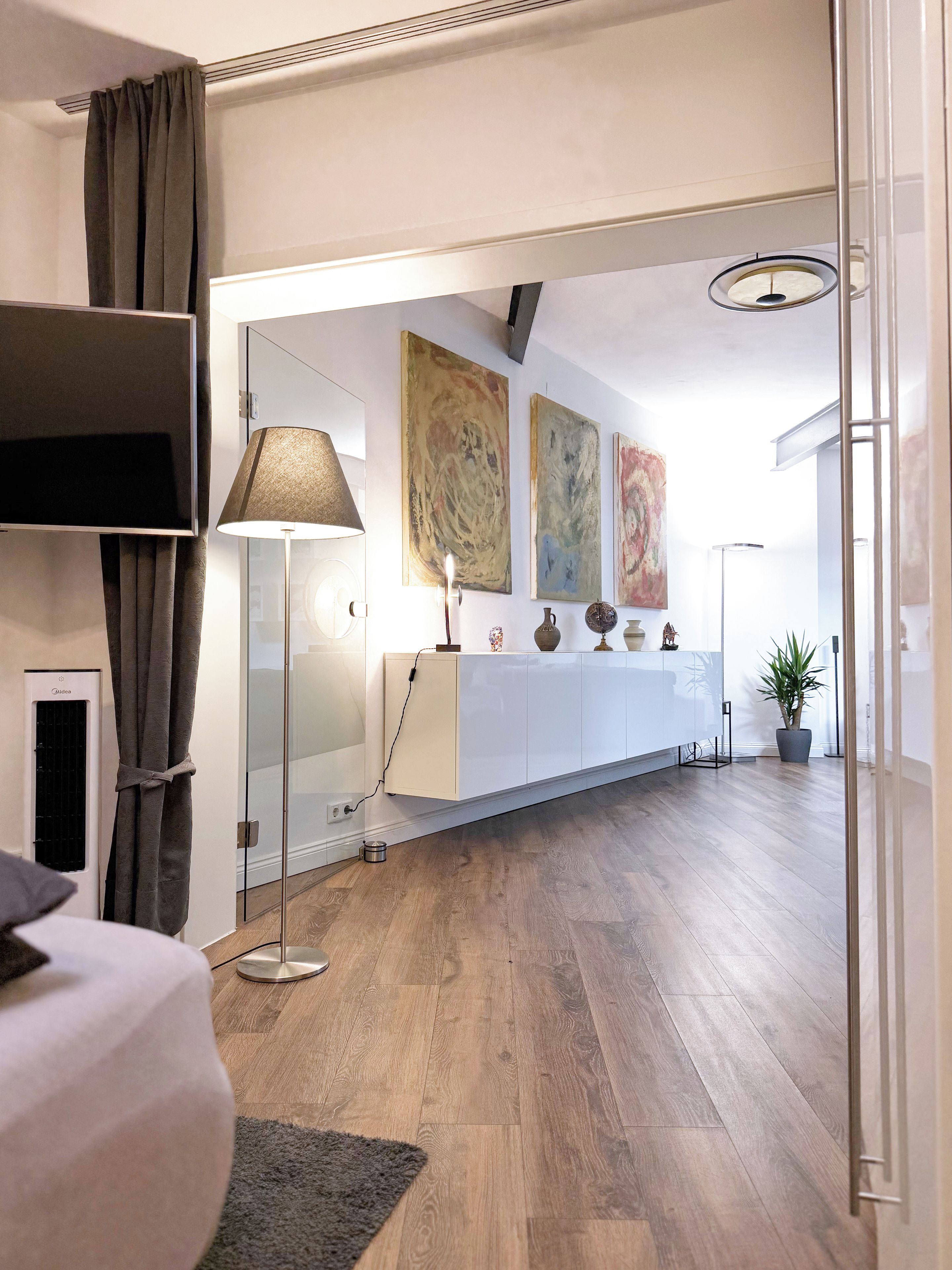 A modern hotel room with a large bed, a bedside lamp, a flat-screen TV, and a view of the hallway.