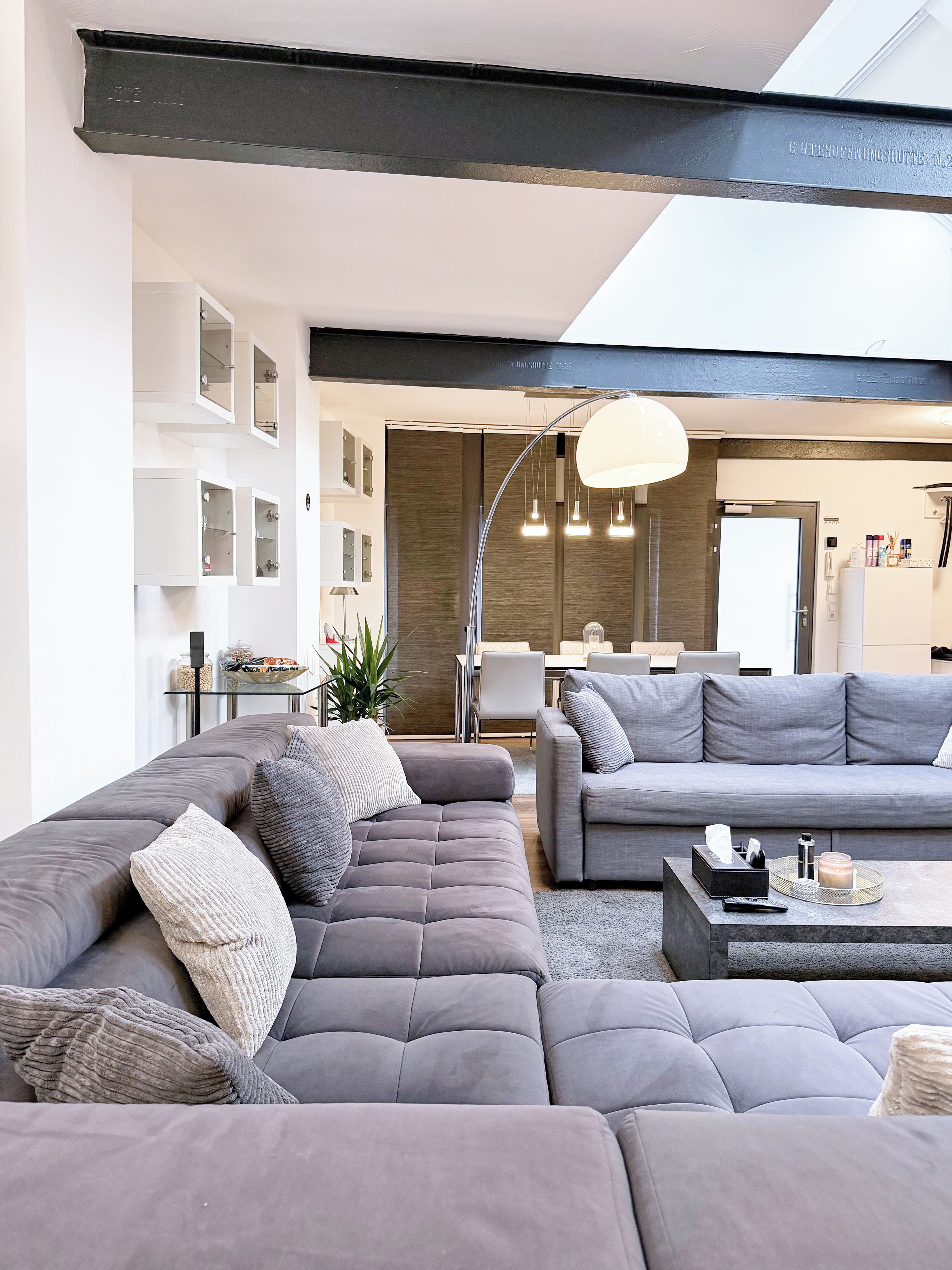 A modern living room with a sectional sofa, a coffee table, and a dining area in the background.