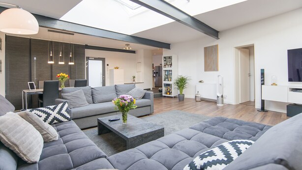 A modern living room with a grey sofa set, a coffee table, and a dining area with a white cabinet.