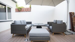 An outdoor patio with wicker furniture, a table, and a large umbrella.