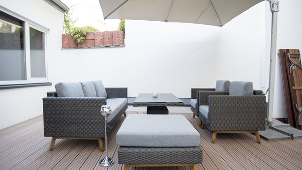 An outdoor patio with wicker furniture, a table, and a large umbrella. - Stylish 168 m² loft in the heart of Düsseldorf (Stadtbezirk 3)