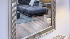 A modern living room with a large mirror, a grey sofa, a floor lamp, and a ceiling with exposed beams. - Stylish 168 m² loft in the heart of Düsseldorf (Stadtbezirk 3)