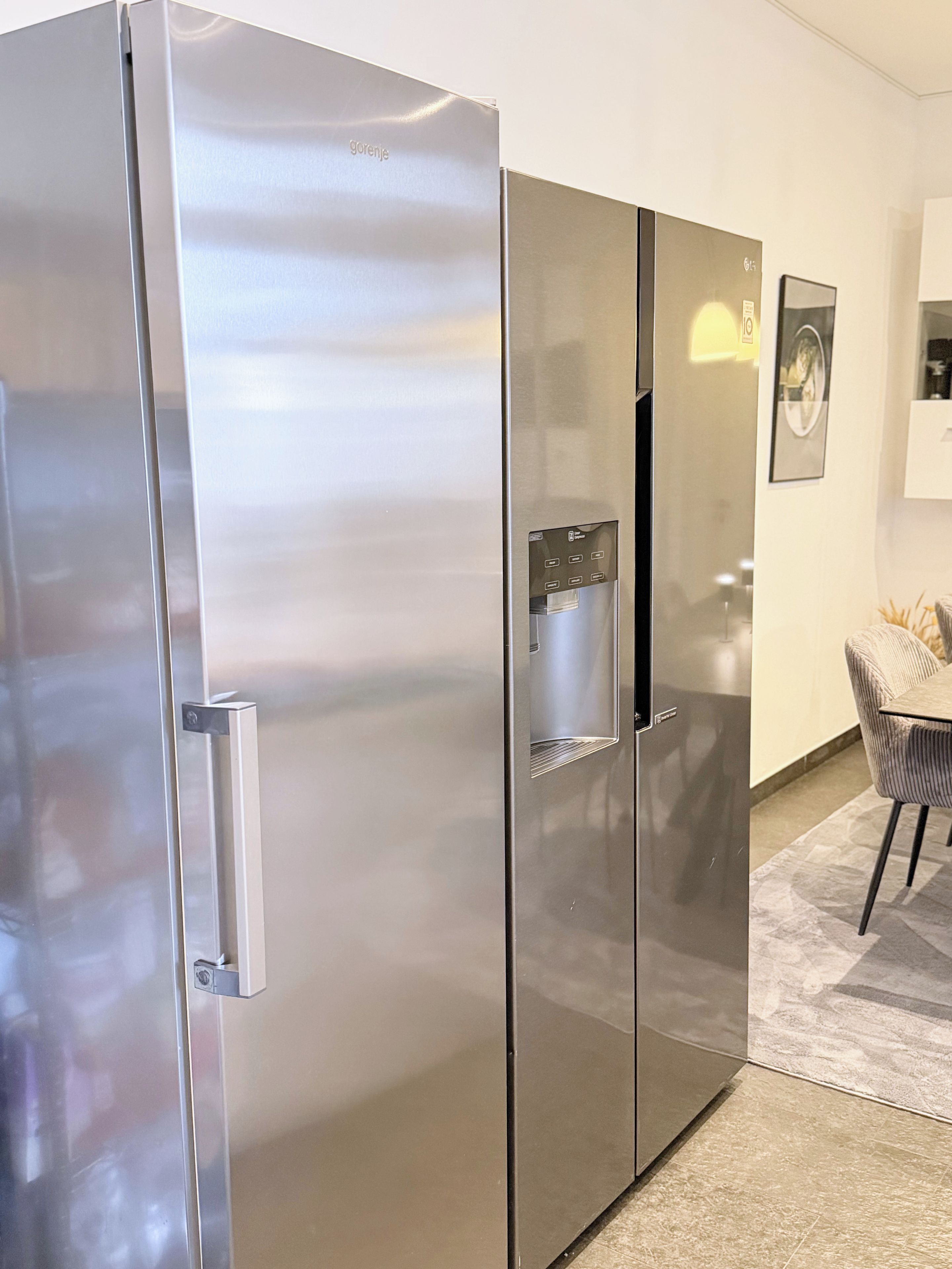 A modern kitchen with a stainless steel refrigerator, a built-in water dispenser, and a dining area with a chair and table.