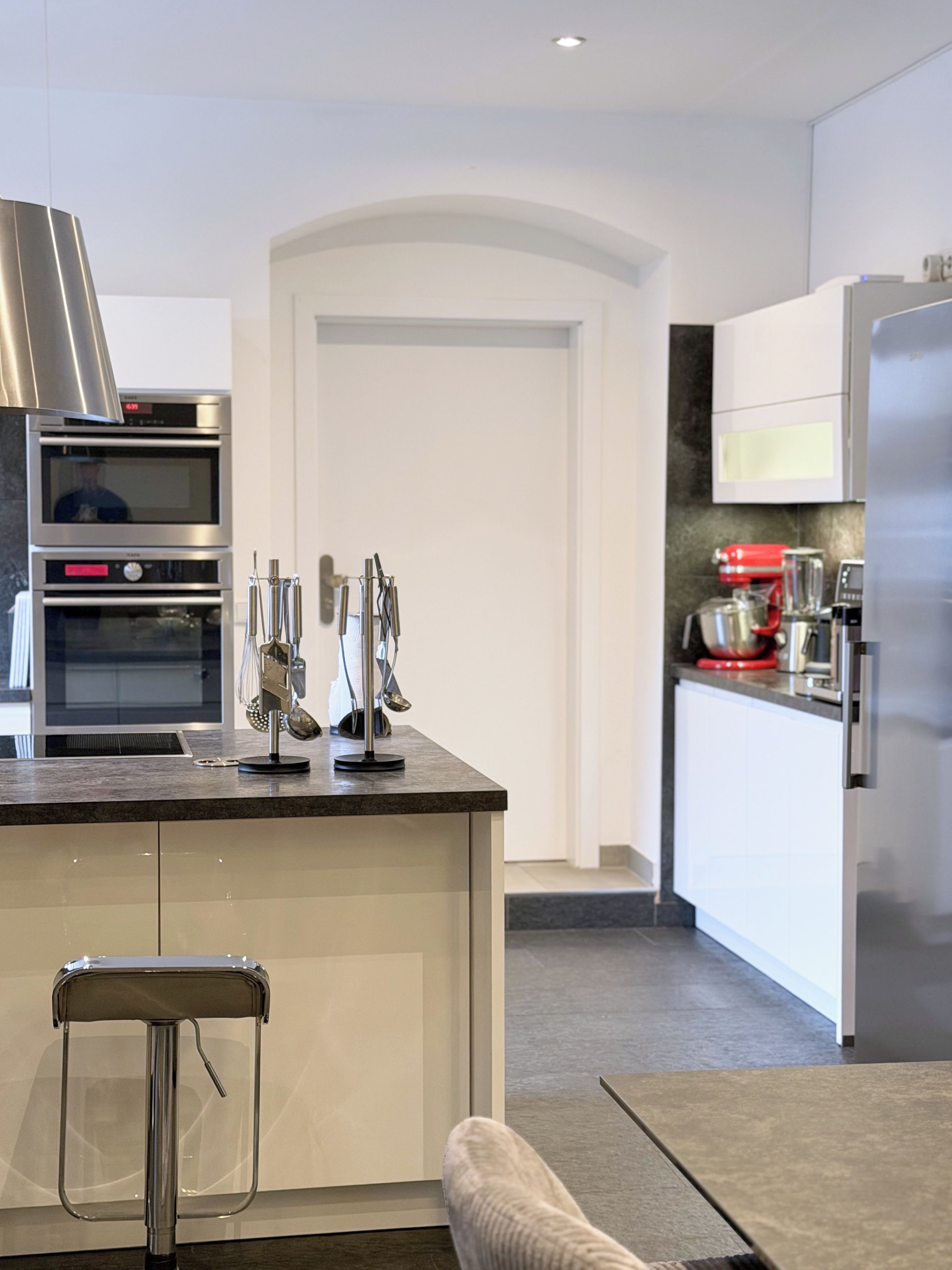 A modern kitchen with built-in appliances, a stainless steel range hood, and a bar stool.
