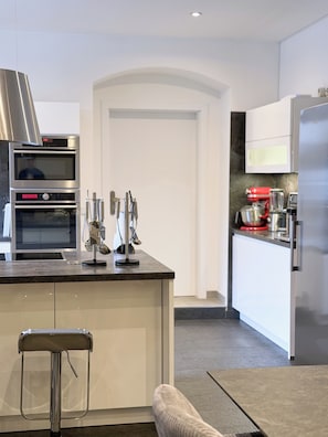A modern kitchen with built-in appliances, a stainless steel range hood, and a bar stool.