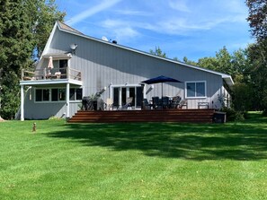 Une maison à deux étages dotée d’un patio couvert, aménagé avec du mobilier d’extérieur et un parasol bleu.