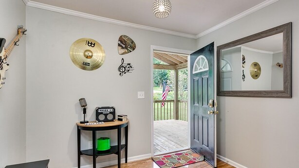 A room with a wooden floor, a black table with a radio and a microphone, a green trash bin, and a door leading to an outdoor area with a wooden deck and a view of greenery. - Down town Travelers rest walking to swamp rabbit bike trail  (Travelers Rest)