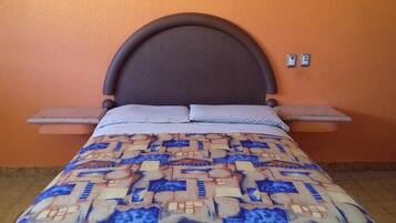 Ein Bett mit gemustertem Überwurf, Kopfteil und Nachttischen vor einer orangefarbenen Wand.