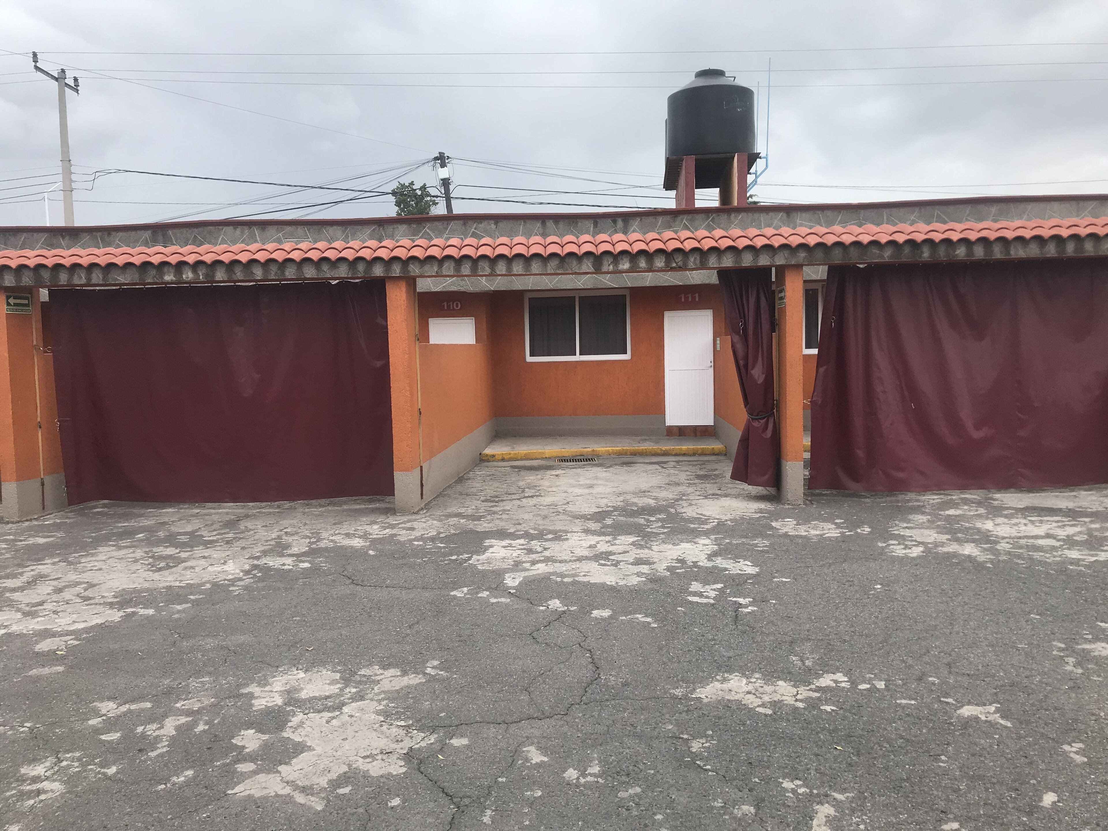 A building with a red-tiled roof, a water tank on the roof, and a closed red gate.