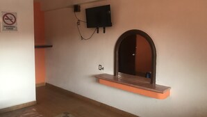 A room with a flat-screen TV mounted on the wall, a small shelf below it, and a door with an arched top. - Motel Tokio Inn (Texcoco de Mora)