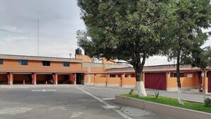 A multi-story building with a parking lot, a tree in the foreground, and a clear sky. - Motel Tokio Inn (Texcoco de Mora)