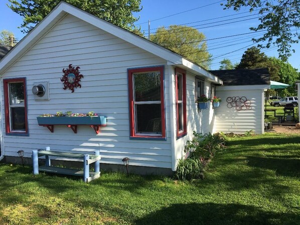A white building with red-framed windows, a bench, and a planter with flowers.