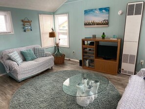 A living room with a sofa, a glass coffee table, a bookshelf, and a television.