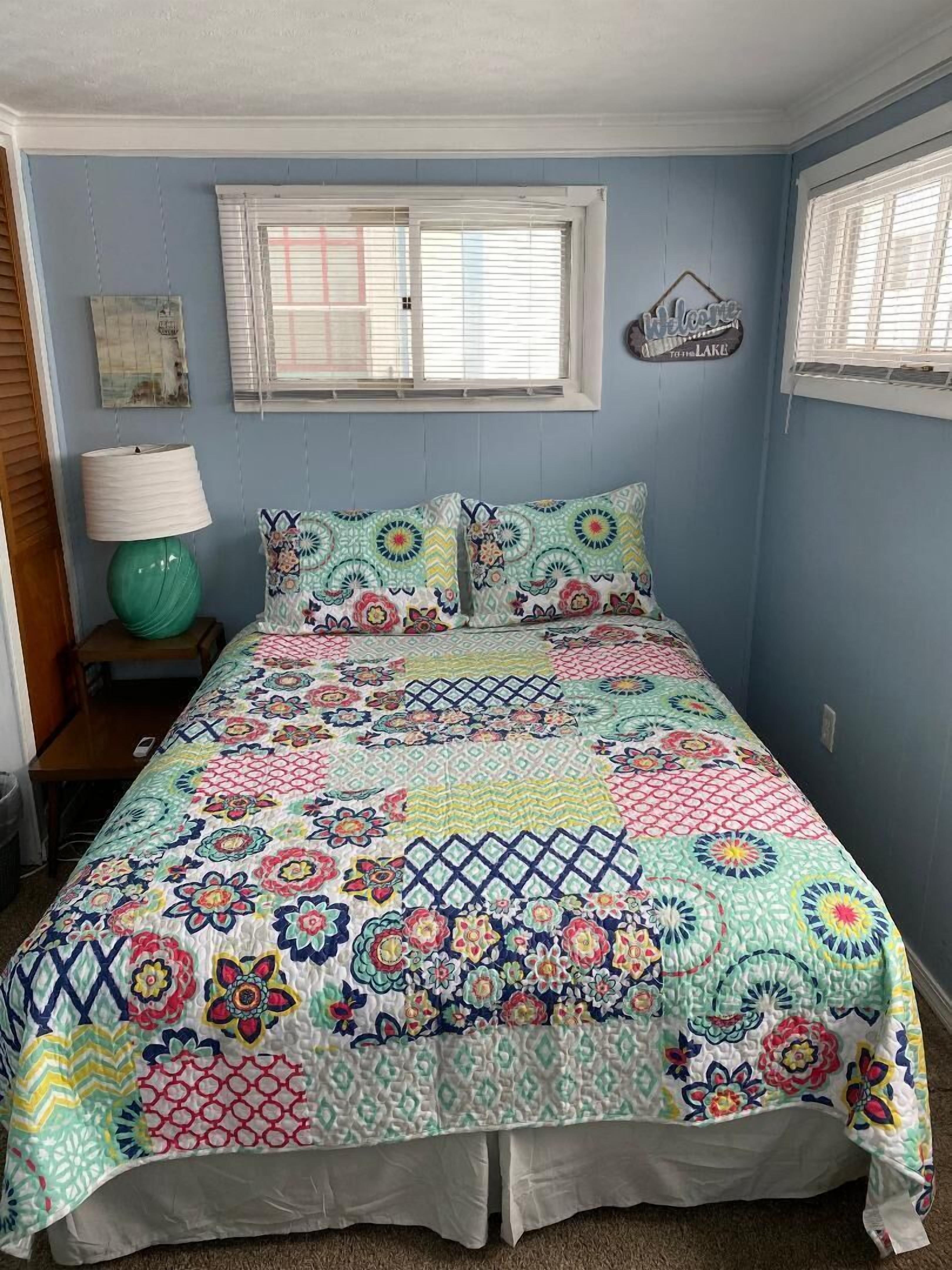 Une chambre à coucher avec une couvre-lit matelassé aux couleurs vives, une lampe de chevet et une fenêtre avec des stores.