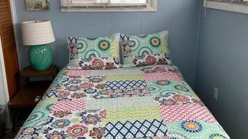Une chambre à coucher avec une couvre-lit matelassé aux couleurs vives, une lampe de chevet et une fenêtre avec des stores.
