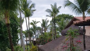 A tropical garden with palm trees, a thatched-roof structure, and a paved walkway. - Pousada Villa Zena (Porto Seguro)