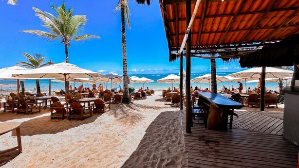 A beachside restaurant with outdoor seating, palm trees, and a view of the ocean. - Pousada Villa Zena (Porto Seguro)