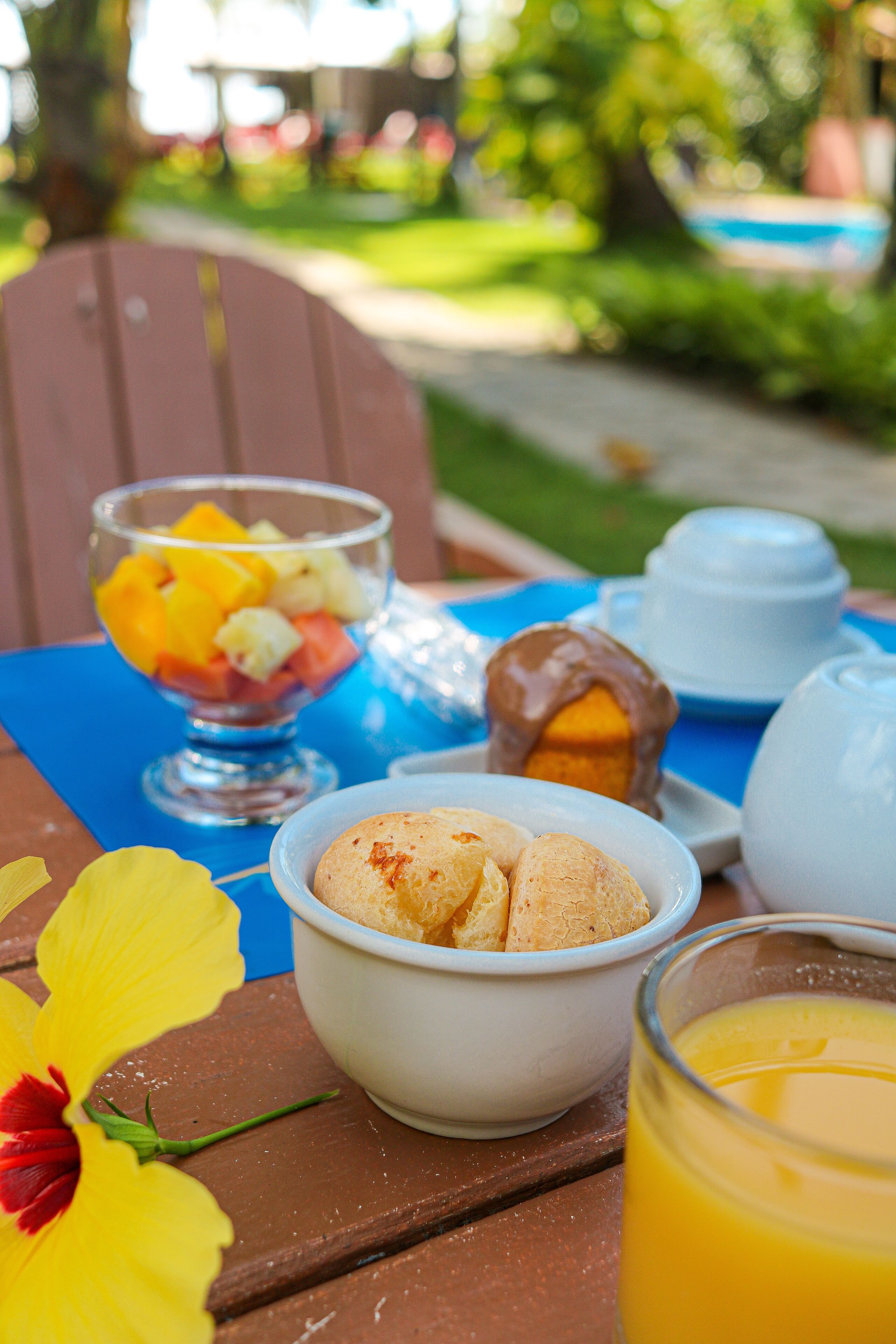 A table with a fruit bowl, a pastry, a teapot, and a glass of orange juice.