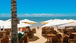 A beachside restaurant with outdoor seating and umbrellas, overlooking the ocean. - Pousada Villa Zena (Porto Seguro)