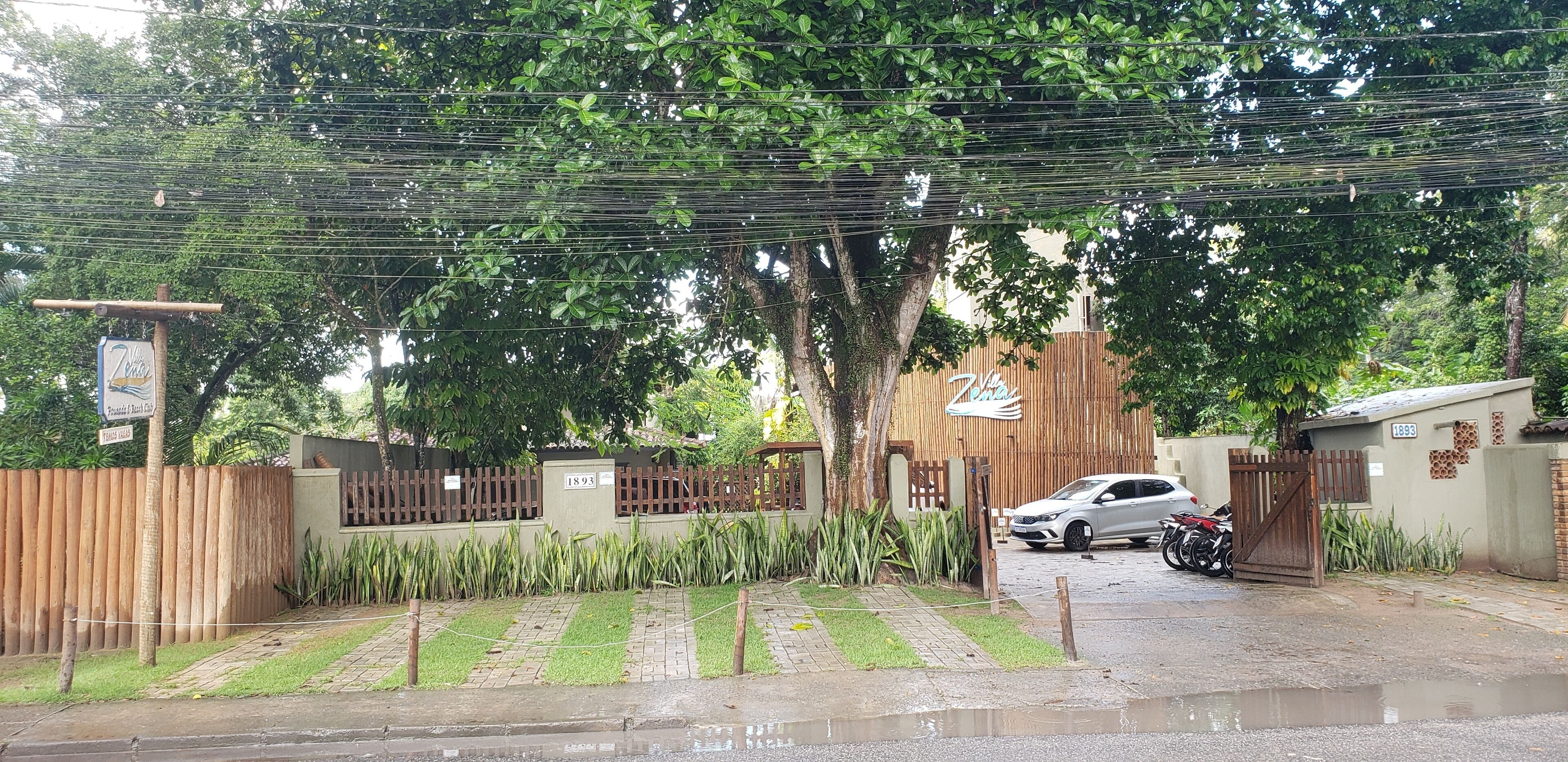 A gated residential area with a paved driveway, parked cars, and a motorcycle.