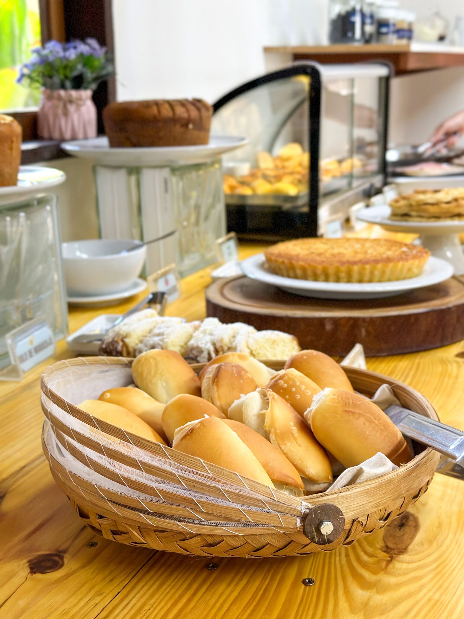 A wooden table with a woven basket containing bread rolls.