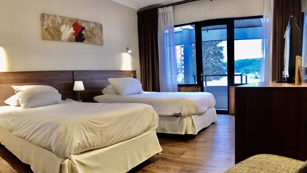 A hotel room with two beds, a desk, and a large window with curtains. - Hotel Turismo Temuco (Temuco)