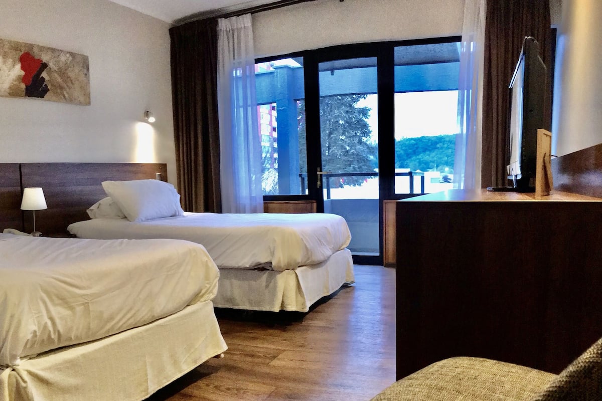 A hotel room with two beds, a desk, and a large window with curtains.