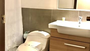 A bathroom with a white toilet, a sink with a mirror above it, and a trash can.