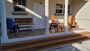 A covered outdoor area with a wooden bench, two wooden chairs, and a table.