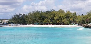 Uma praia com águas turquesa cristalinas, areal arenoso e uma floresta densa ao fundo.