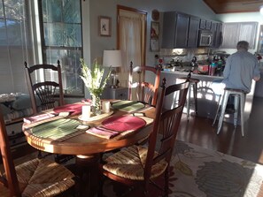 A dining area with a round table, chairs, a vase with greenery, and a kitchen in the background. - Peaceful Lakefront Getaway, Stunning Sunsets & Waterfront Relaxation (Keystone Heights)