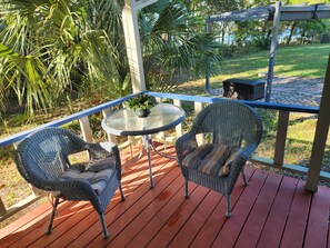 A covered patio with wicker chairs and a glass table, surrounded by greenery and a view of a grassy area. - Peaceful Lakefront Getaway, Stunning Sunsets & Waterfront Relaxation (Keystone Heights)